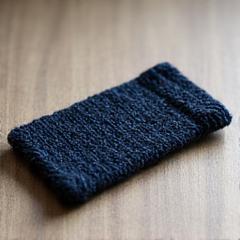 Knitted phone case with a unique texture, lying on a wooden table.